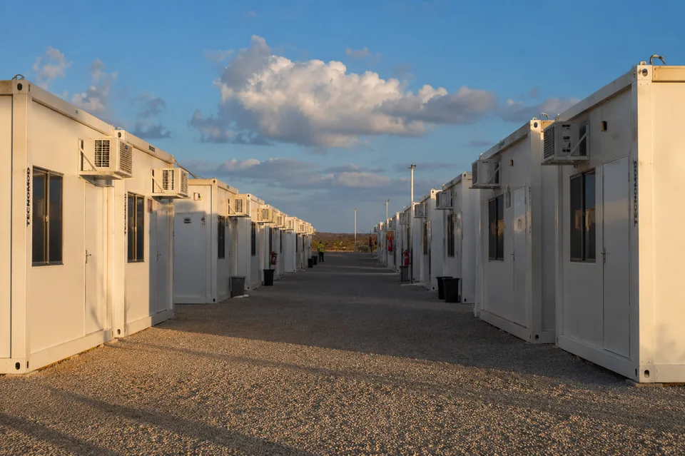 Fileira de módulos habitáveis Tecnomod instalados em canteiro de obra sobre base de brita, ao entardecer