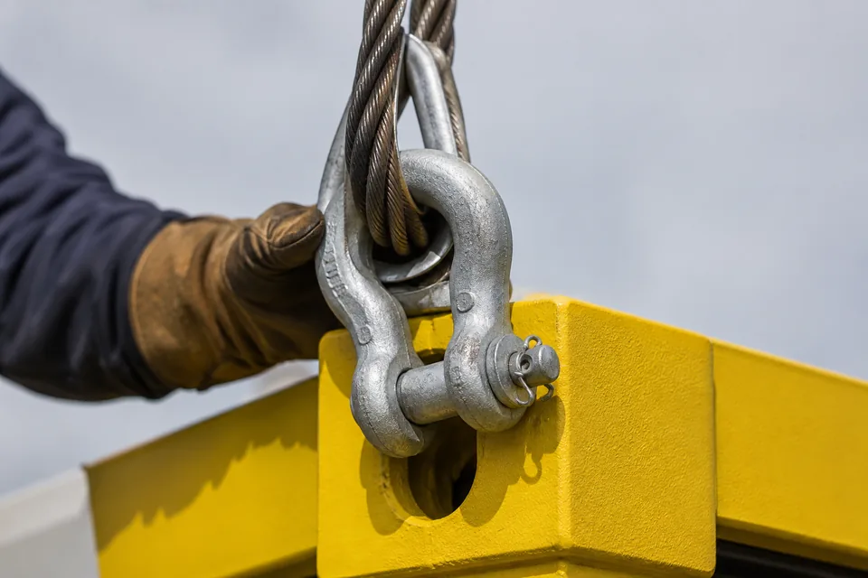 Detalhe da manilha do conjunto de slingas conectada ao bloco de canto amarelo do módulo offshore