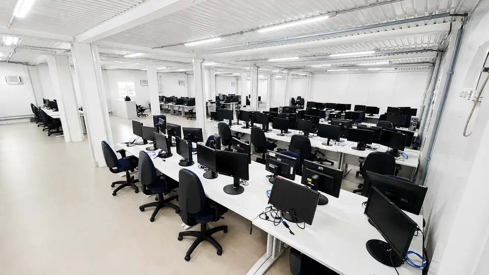 Open space modular com fileiras de bancadas, cabeamento estruturado e pilares de junção entre módulos