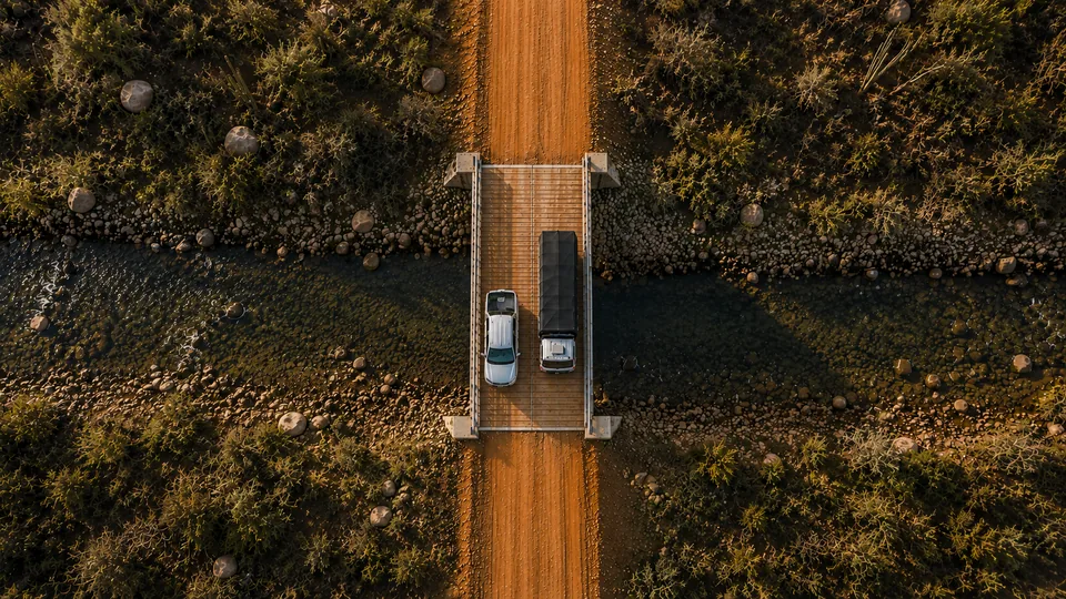 Vista aérea vertical da ponte modular dupla, com dois veículos lado a lado e a junta central dividindo o tabuleiro