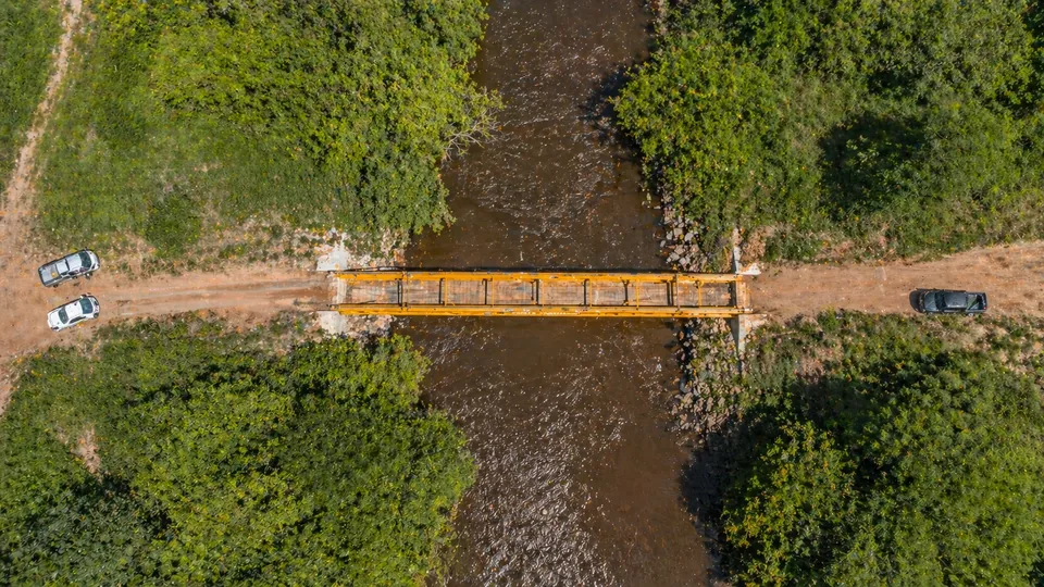 Vista aérea vertical da ponte modular Ponte Pronta ligando os dois trechos de uma estrada de terra sobre o curso d'água