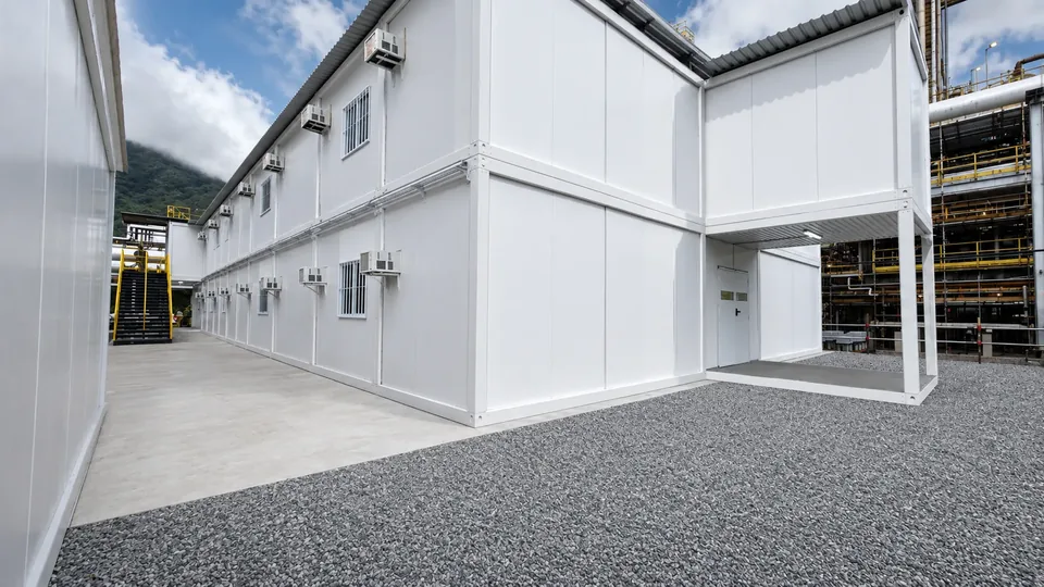 Prédio modular de dois pavimentos em L montado em pátio industrial, com cobertura metálica e drenagem em brita