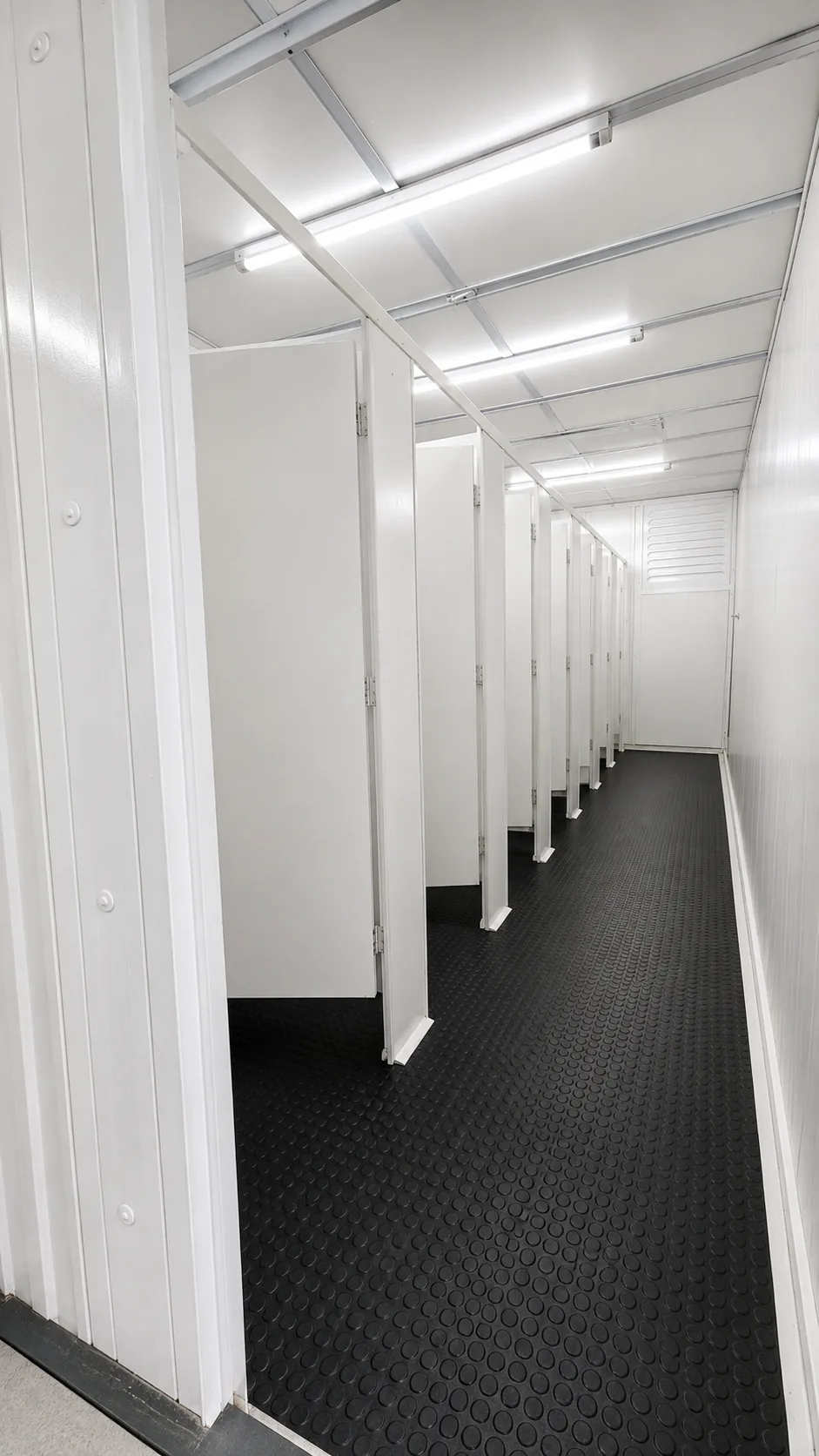 Corredor de cabines sanitárias em módulo, com piso antiderrapante e ventilação forçada